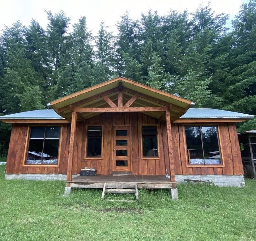 Fachada de una cabaña de madera con porche central y grandes ventanas